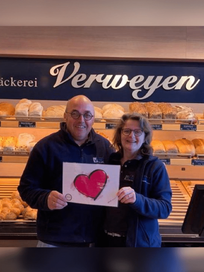 ein Mann und eine Frau halten zusammen ein Schild mit einem roten Herzen drauf